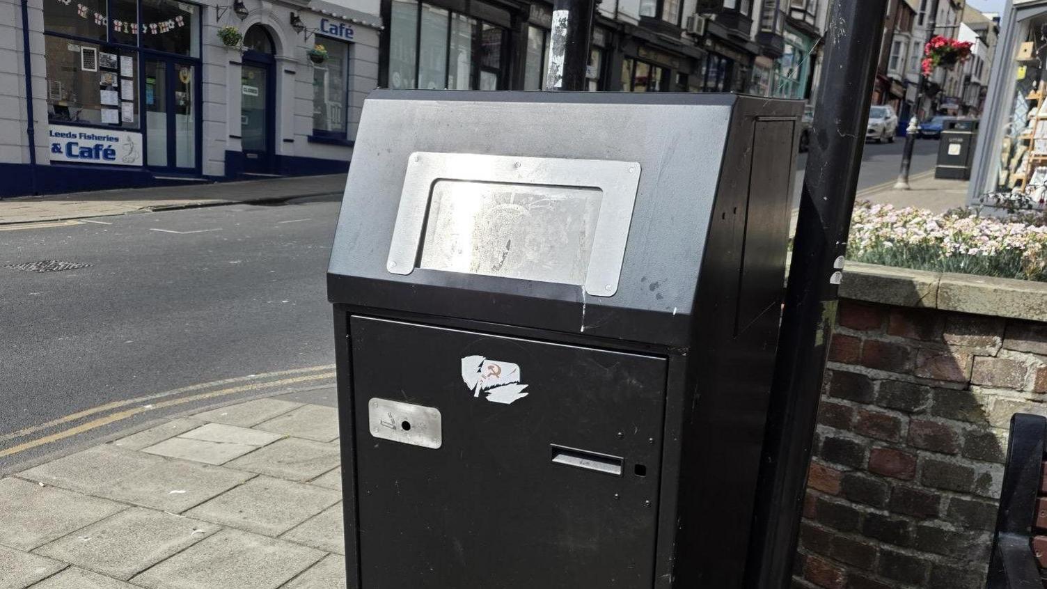 A black bin with a metal opening on a high street.