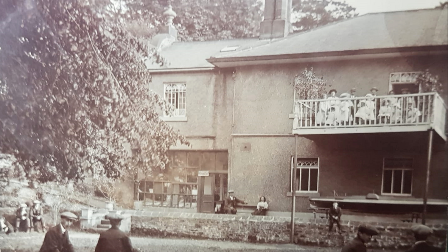Another historic photo of the spa, which shows people sat on an outdoor balcony, with children wearing flat caps sat on the ground below them.