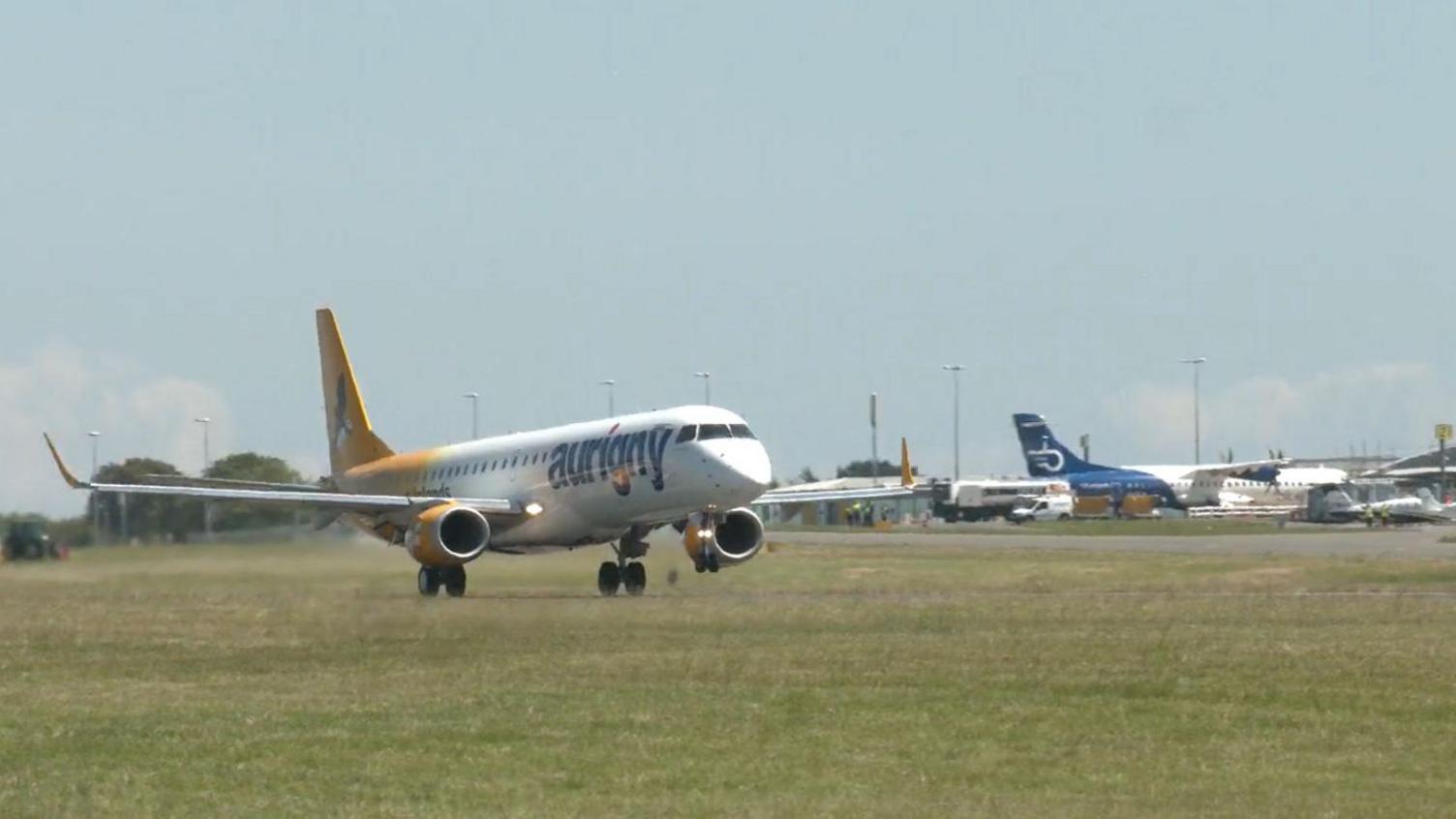 A white plane with jet engines with the word Aurigny on its nose taking off from Guernsey's airport runway.