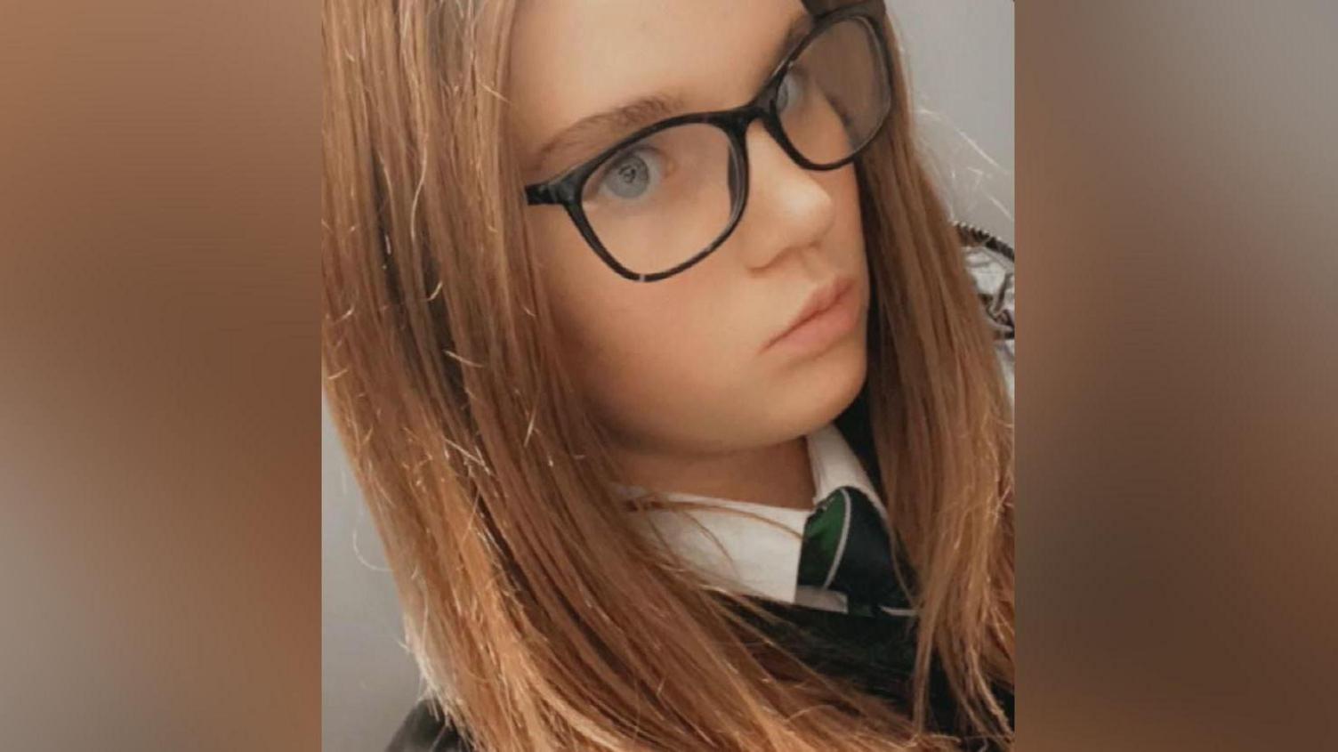 A girl in a school uniform with glasses and long dark hair takes a selfie