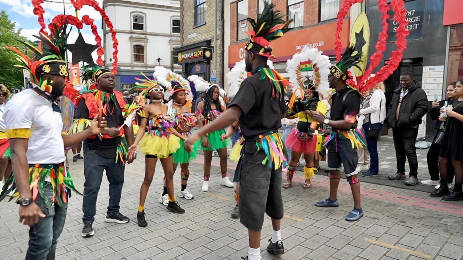 A group of dancers wearing costumes are stood together on a street in Luton