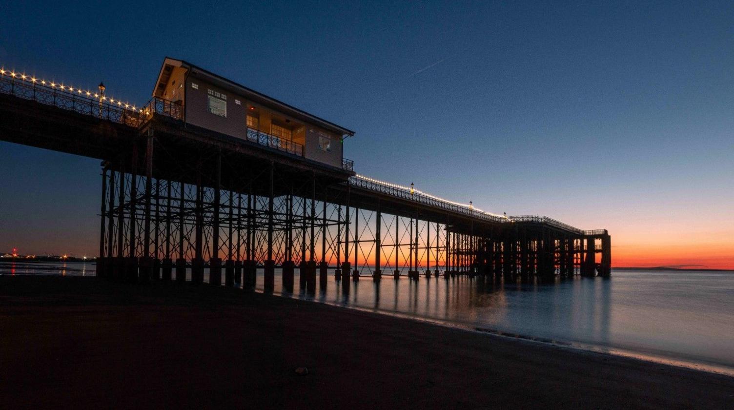 Penarth pier, shot from the beach. The photo has been taken early in the morning, with the pier in darkness and the sea and sunset behind