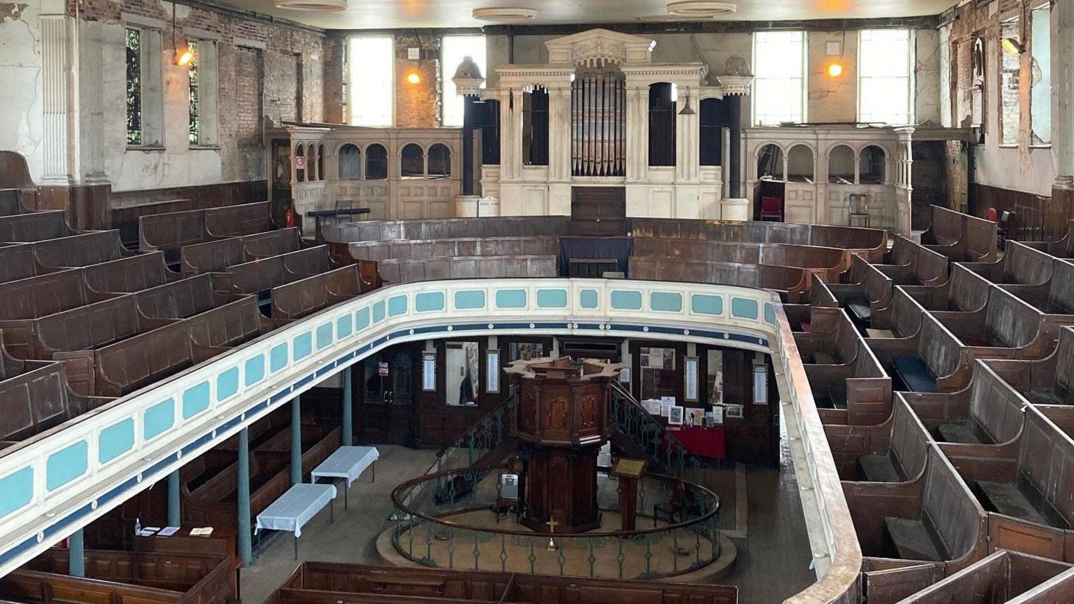 The first floor gallery has an organ at the front and pews around the side, and the ground floor area, which has more pews facing a pulpit, is visible below.