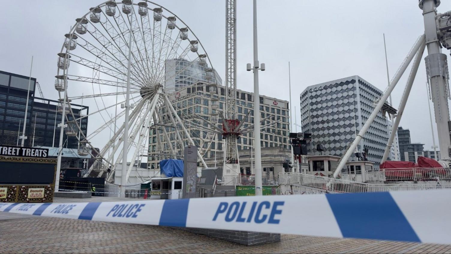 Blue police tape in the foreground, behind which the deserted City Star Flyer ride is visible, as well as a ferris wheel and office buildings.