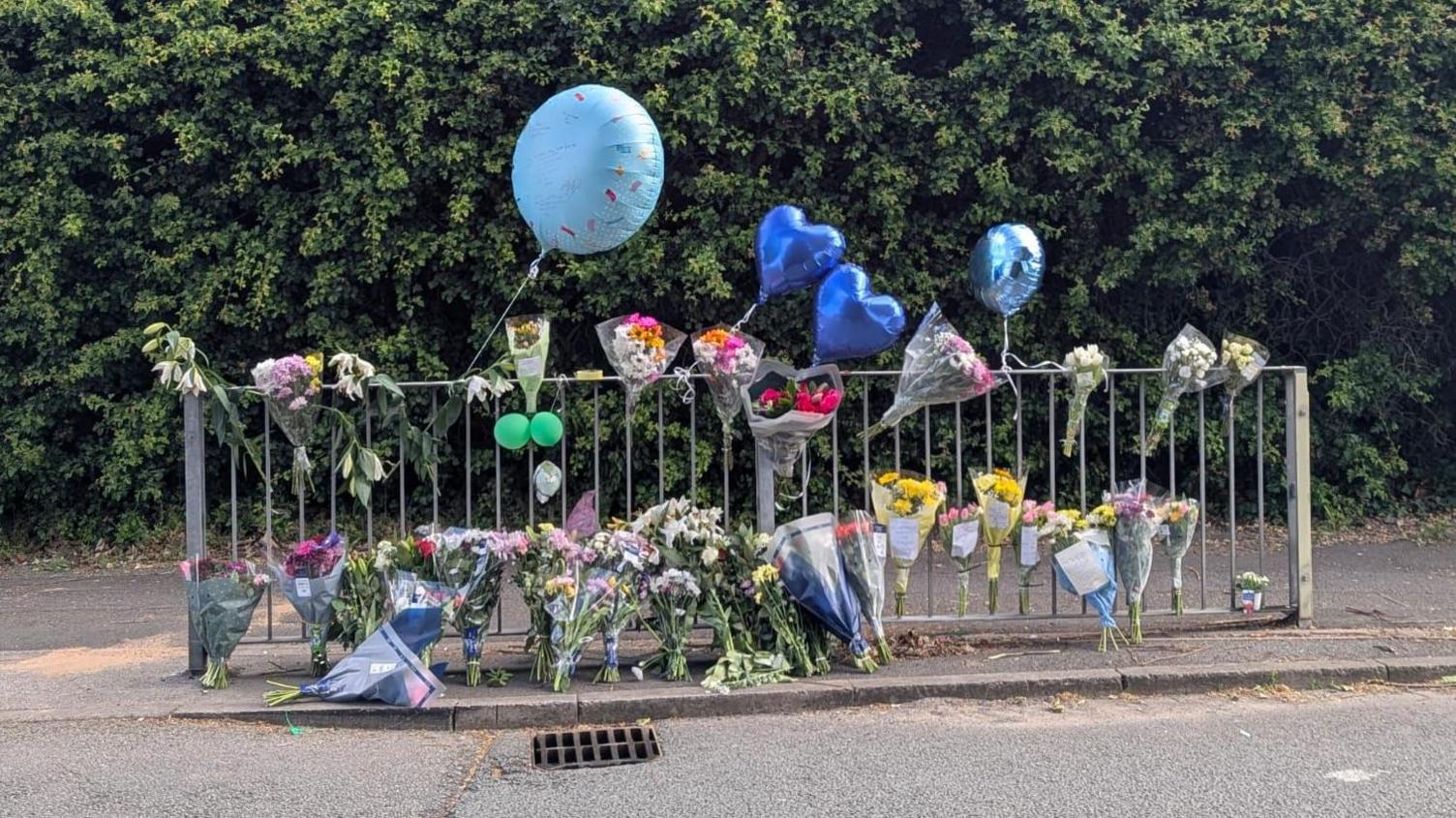 Flowers and balloons next to a metal barrier on the side of the road.