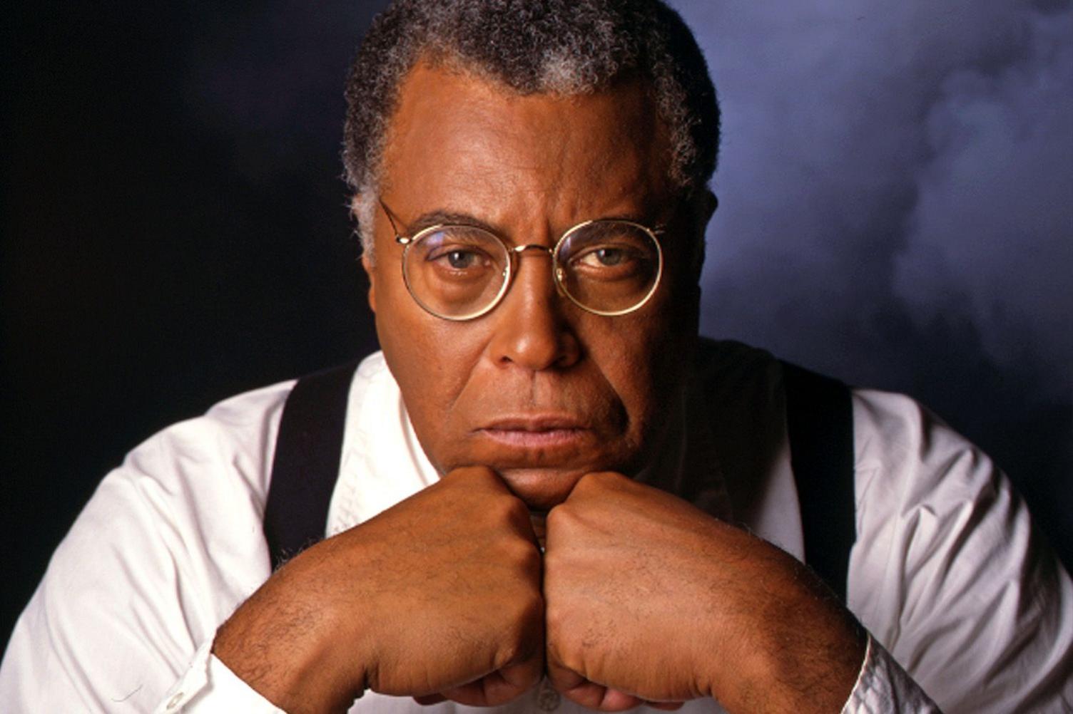 A bespectacled James Earl Jones stares in to the camera with his chin resting on his fists. He is wearing a white shirt and braces.