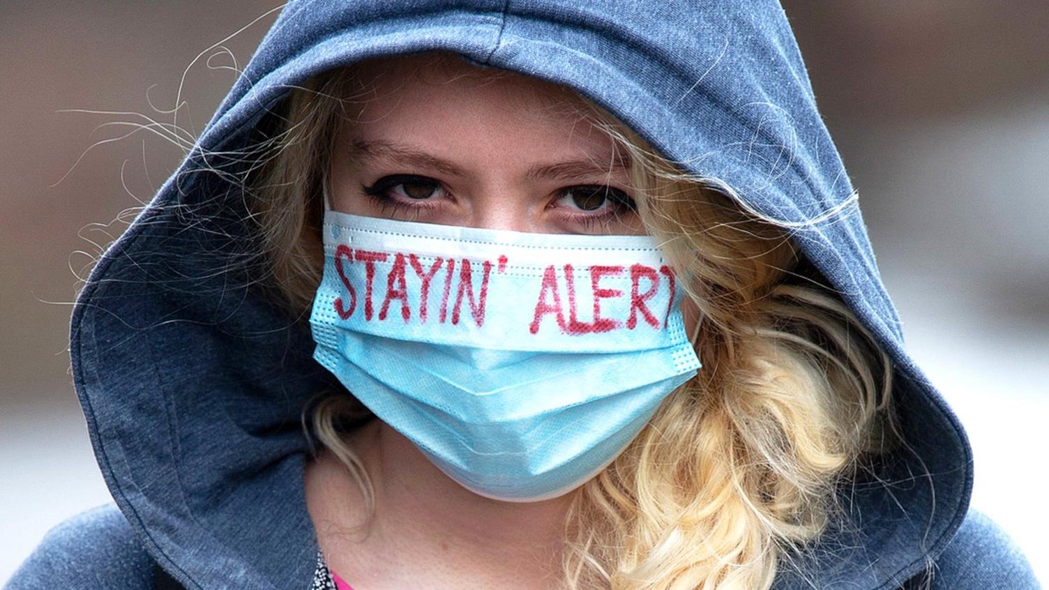 Young woman wearing a face mask with the words "stayin' alert" on it