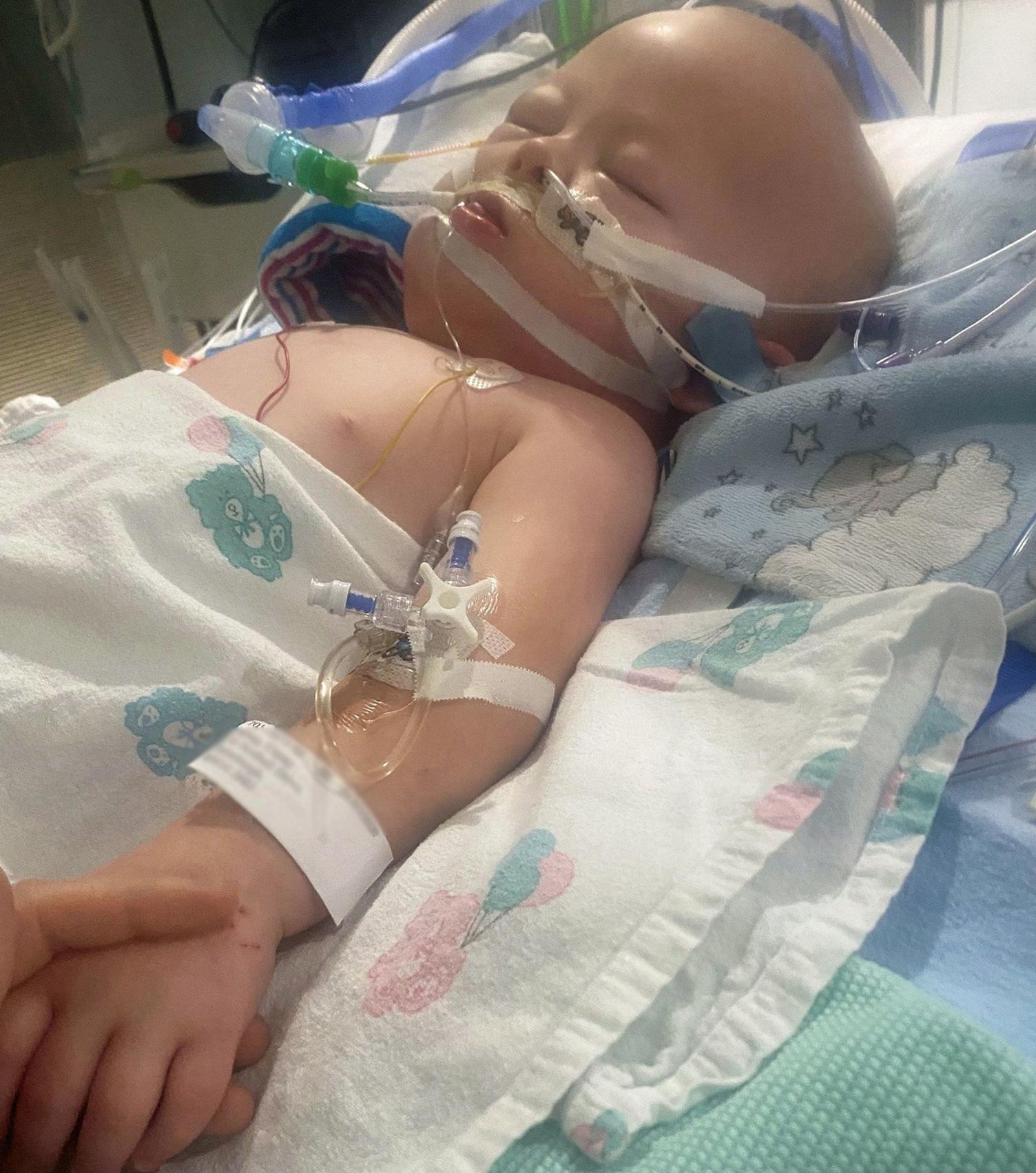 Corey lying in hospital bed with a parent holding his hand.