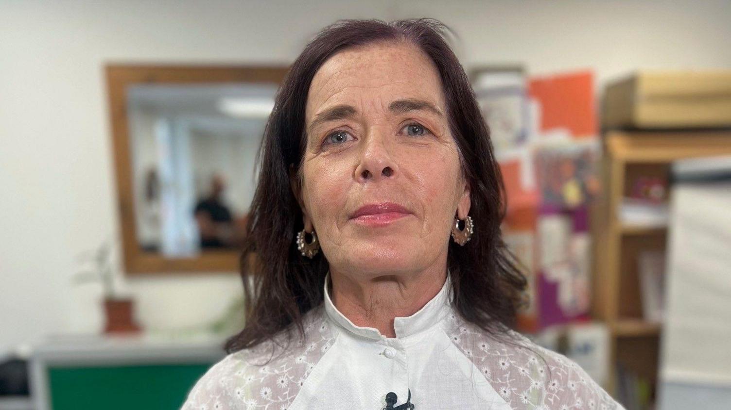 Silvia Petretti in a white dress. She has shoulder length brown hair and wears silver-coloured hoop earrings. 