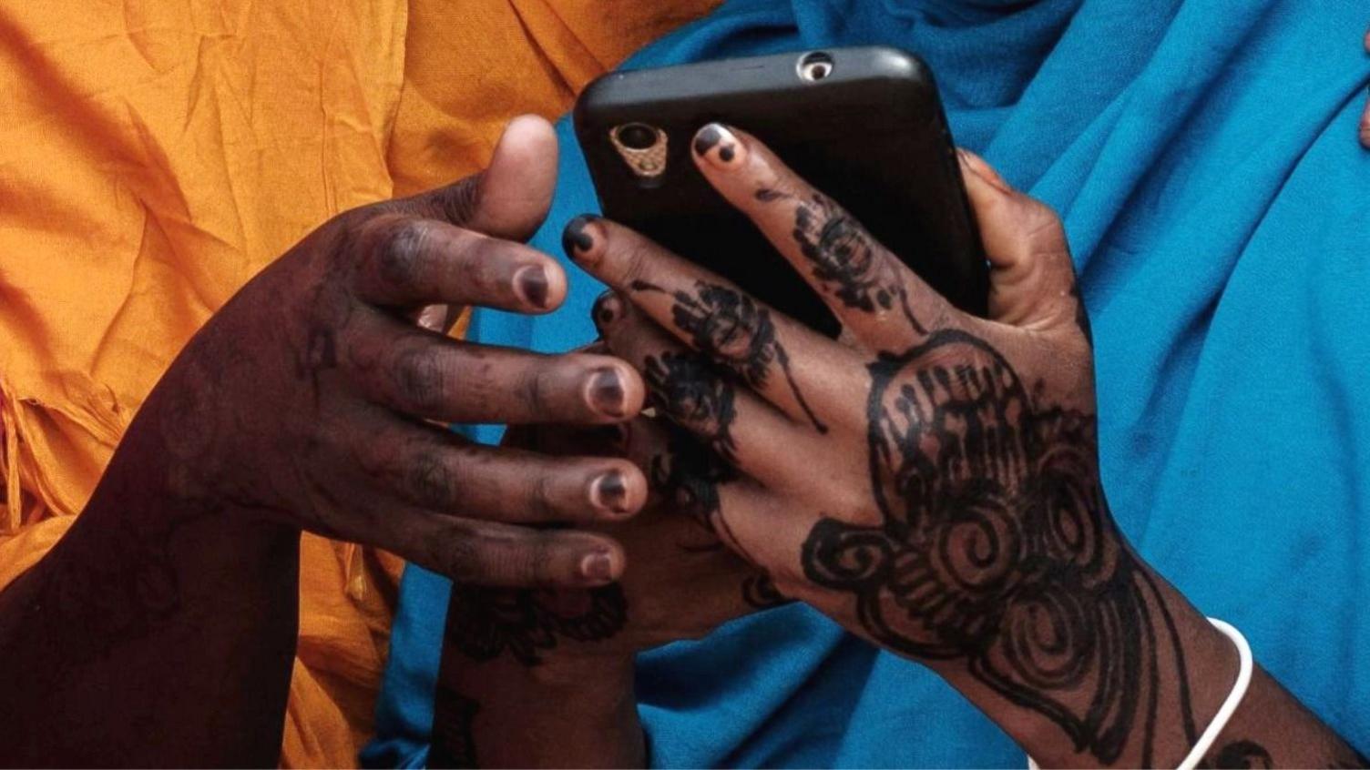 A close up of a young woman from Somalia with hennaed hands holding a mobile