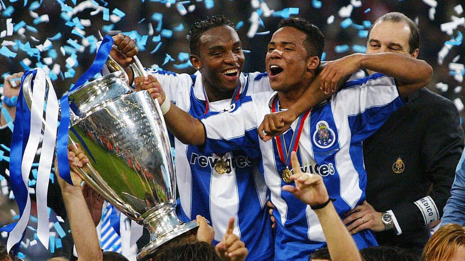 Benni McCarthy and Porto team-mate Carlos Alberto, wearing blue and white vertical-striped Porto shirts with medals around their necks, celebrate with the Champions League trophy as ticker tape falls around them.