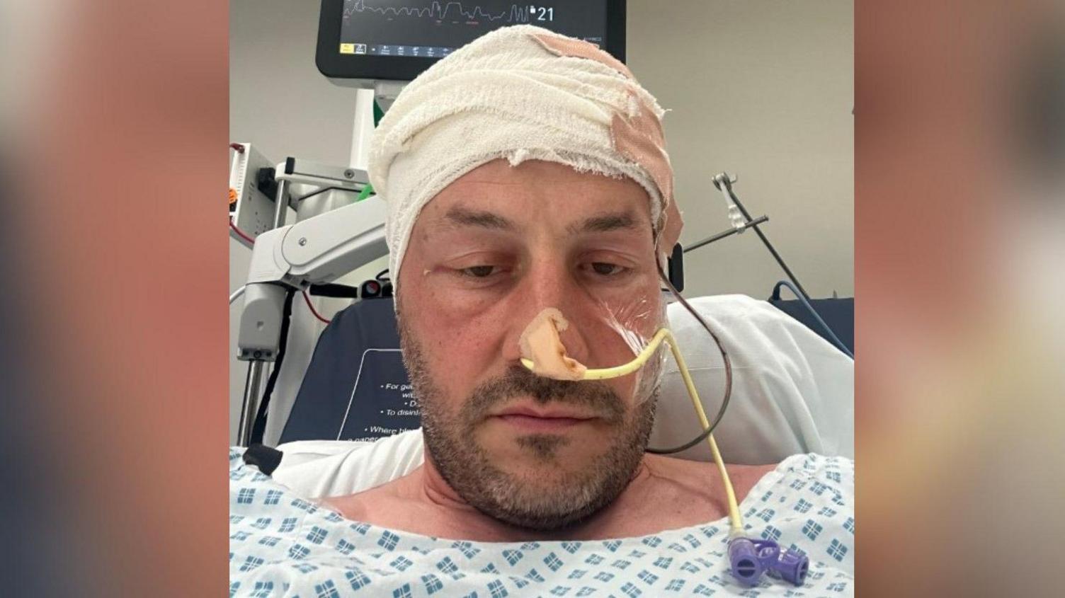 George Wade in a hospital bed with a bandage on his head and tube in his nose
