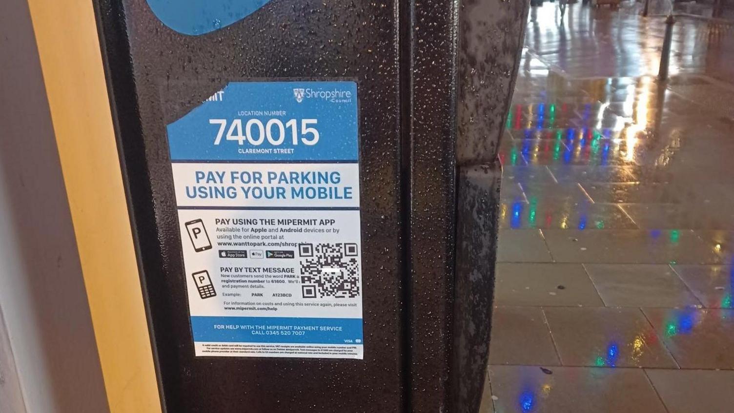 A blue and white council sticker on the side of a black pay and display parking machine. On the sticker, there is a black QR code