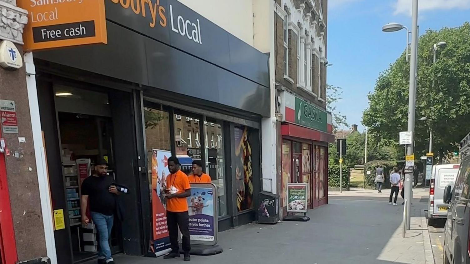 Three people stand outside a Sainsbury's Local store in Leyton, east London