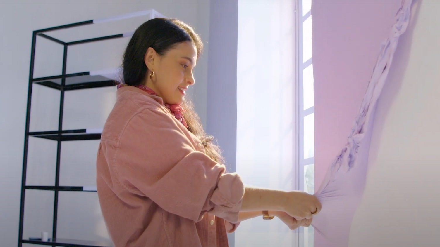 A women peels lilac-coloured paint off the wall. 