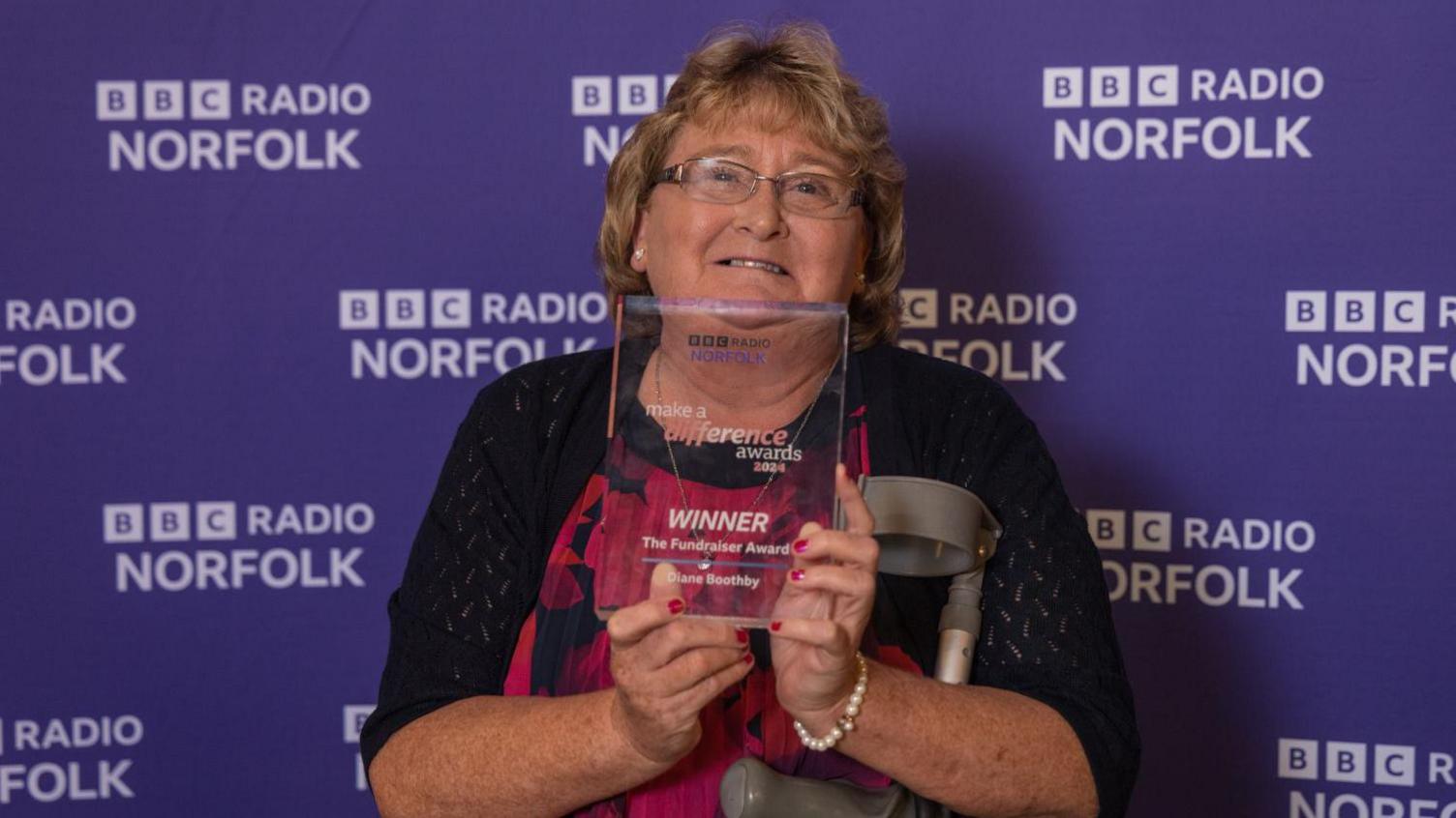 Diane Boothby wearing a black and red dress holding her Make a Difference glass award.