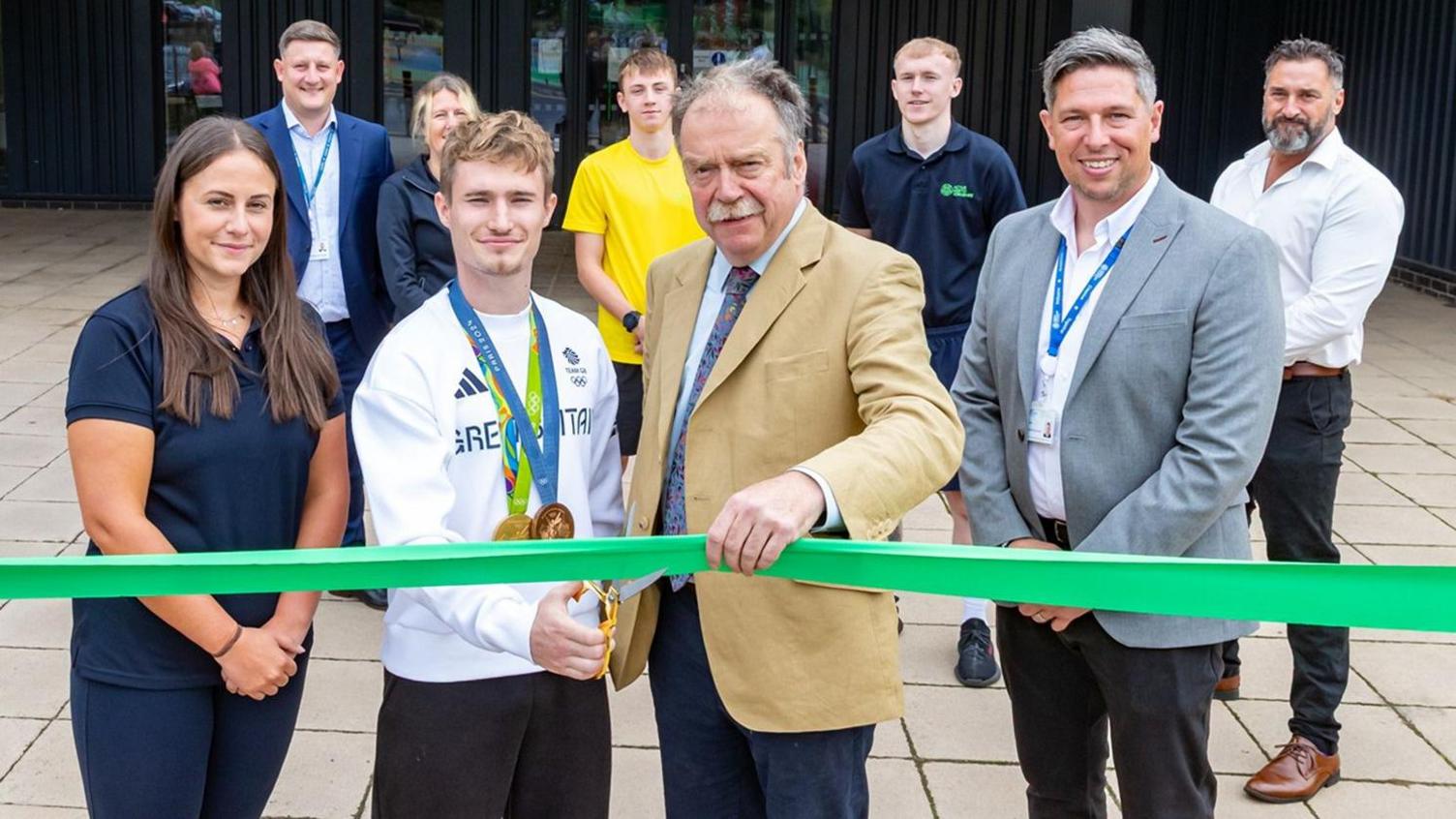 Jack Laugher, Olympic diver, cuts a green ribbon to open Ripon's leisure centre, with other officials standing beside him.