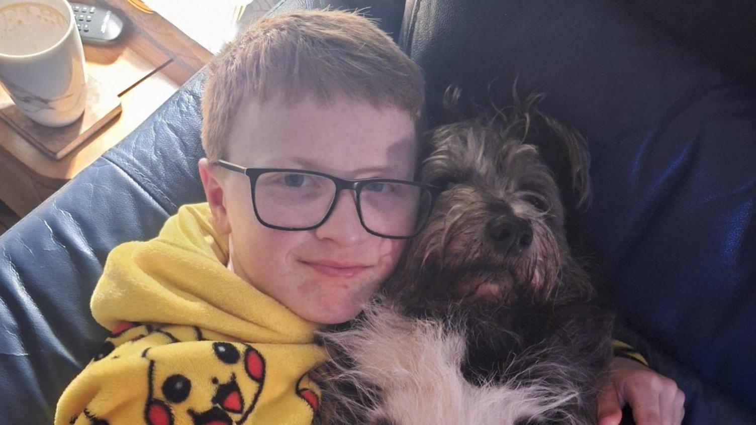 Tommy wearing glasses, a pikachu hoodie and hugging a dog on the sofa.