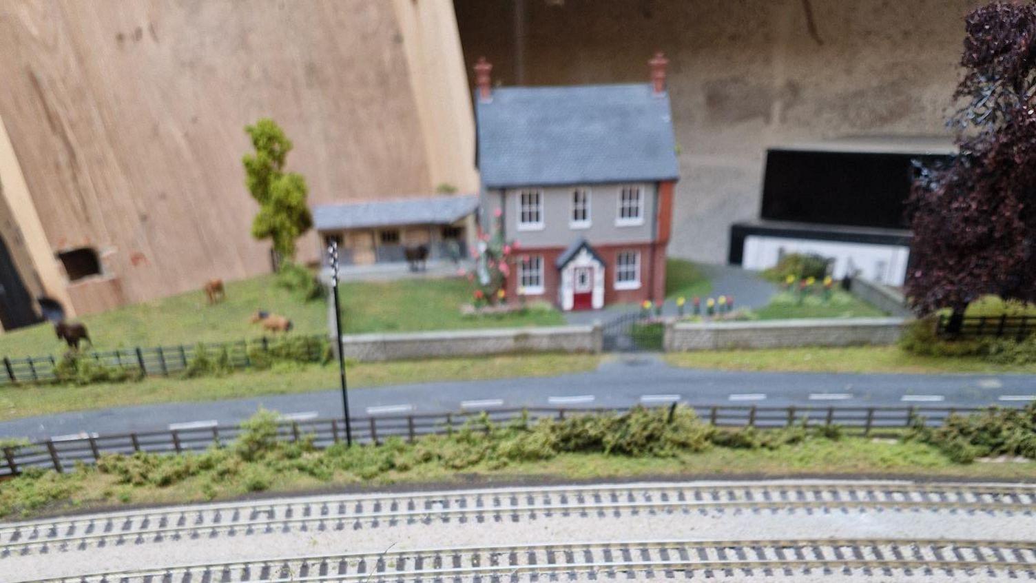 Model railway scenery, including grass, trees, fences, and a house