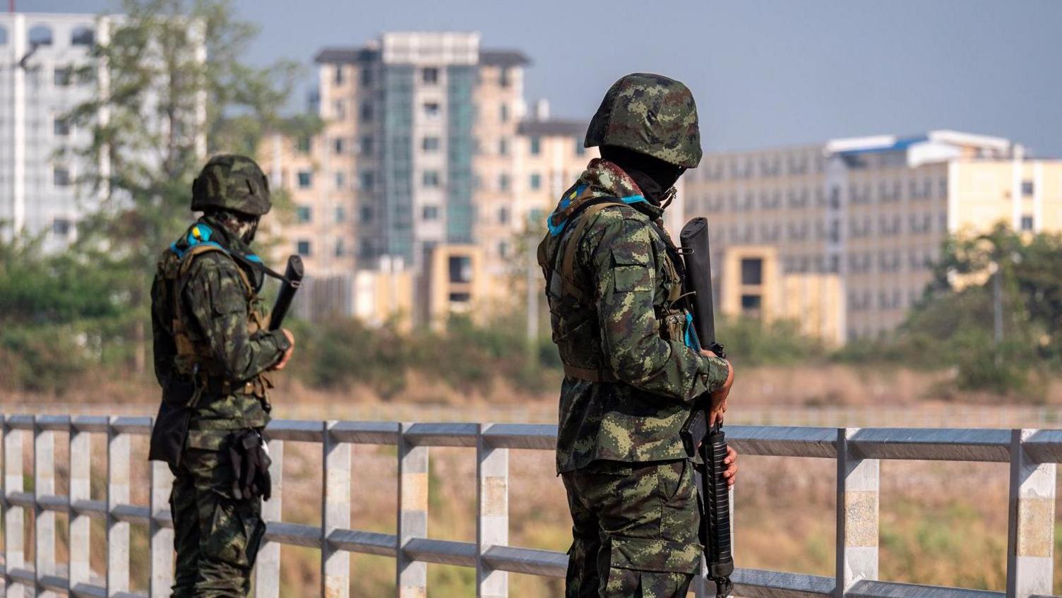 Tall buildings in Myanmar's Myawaddy seen from Thailand's border, where armed guards stand on a bridge  