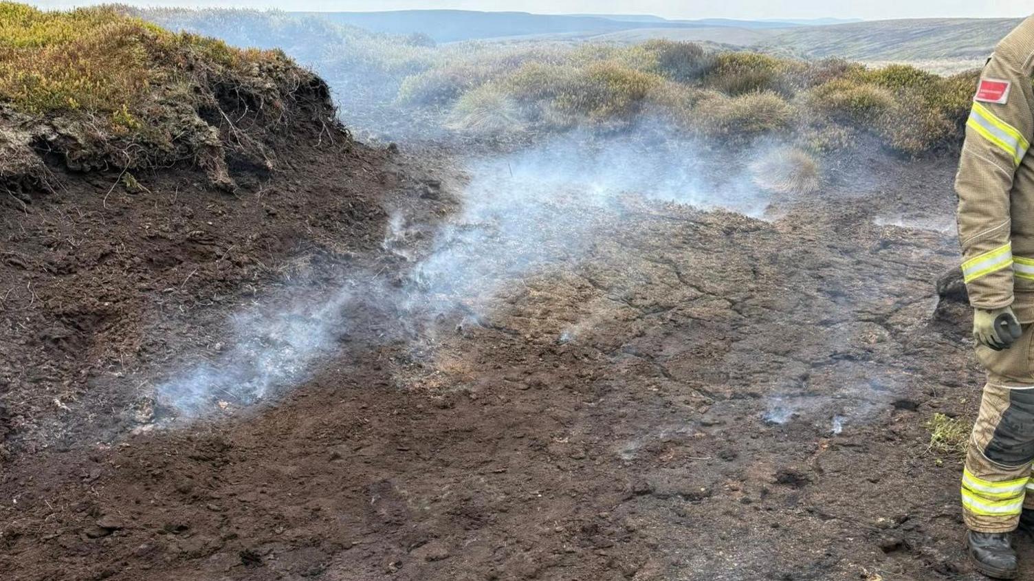Smoke in the countryside with a firefighter to the right of the image.
