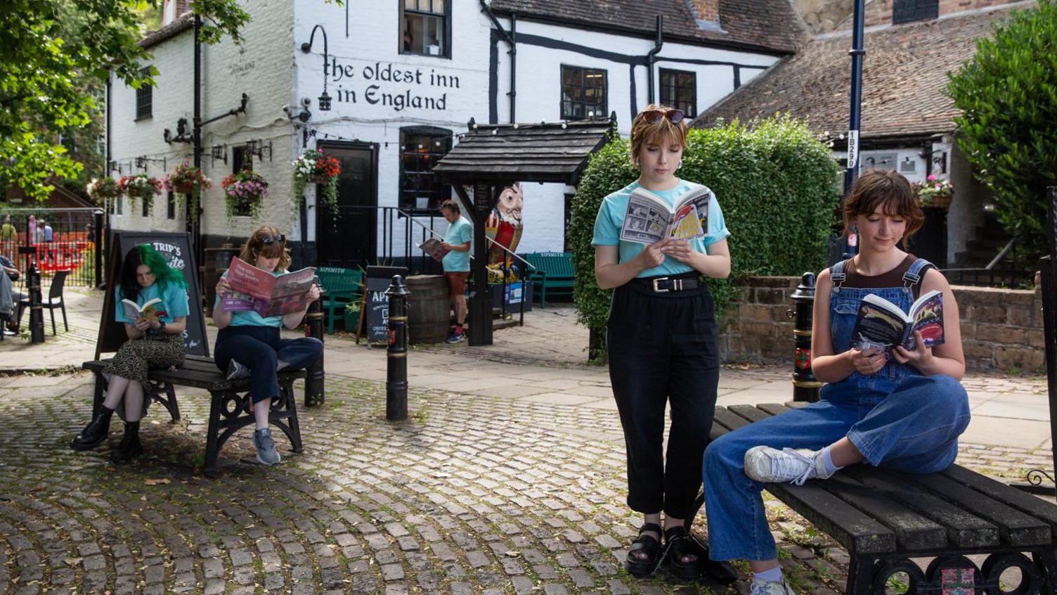 A photograph of four young people reading books, with three sitting on benches