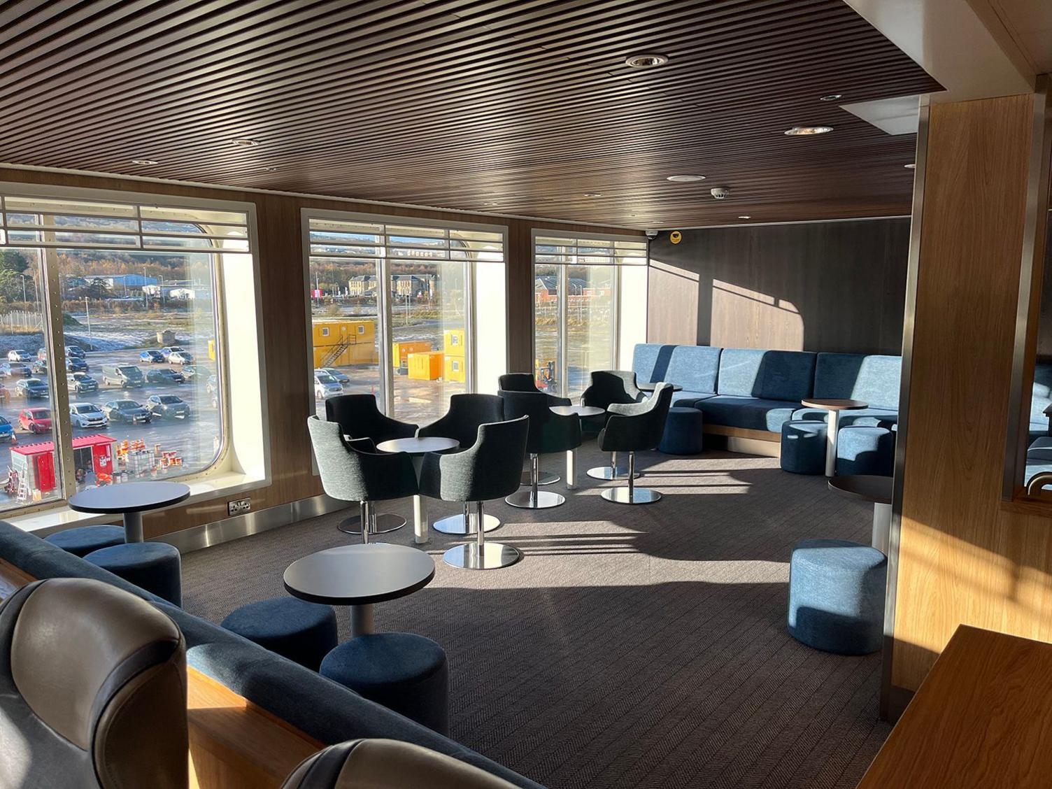 Blue seats around small round tables next to the side windows of the internal passenger area of Glen Sannox