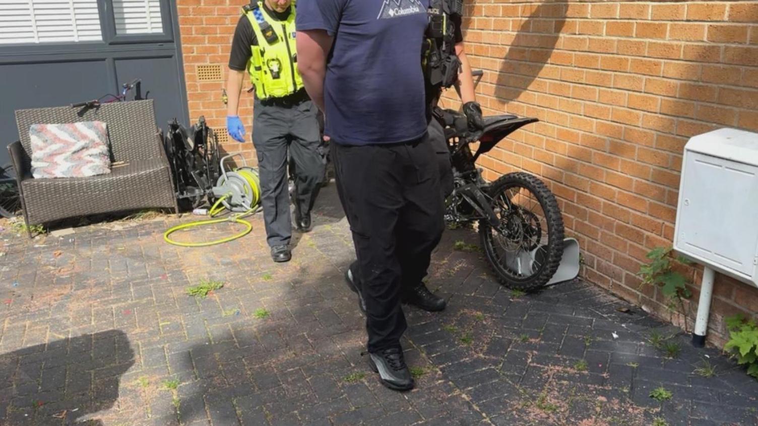 Police officer escorting a handcuffed man out of a property. Their faces are not pictured