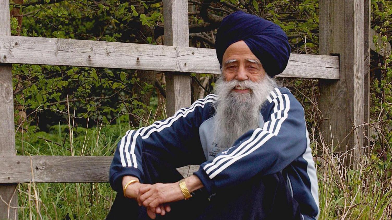 Fauja Singh rests after a run near his home in Ilford, England, Saturday, April 10, 2004. He's wearing a blue tracksuit and sitting with arms folded, smiling at the cameras.