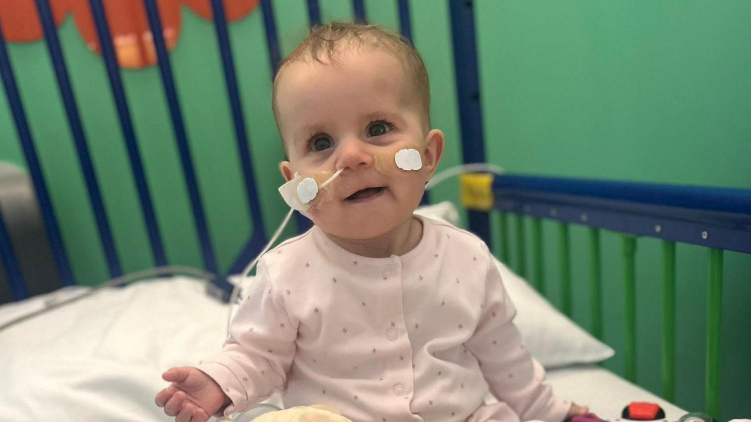 Baby Isla in hospital in a cot sat up 