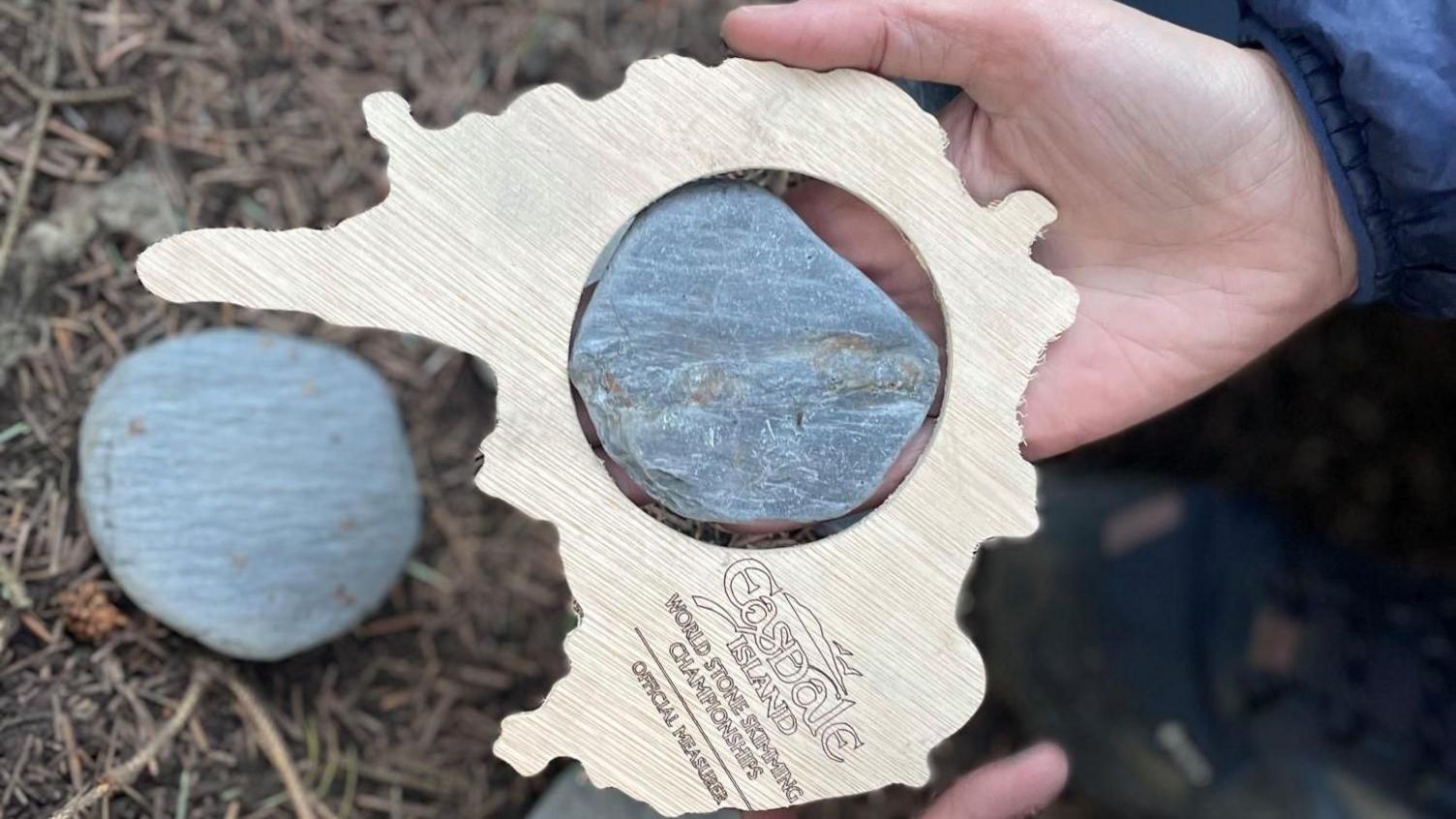 A stone slate is held up inside a circular wooden measuring device