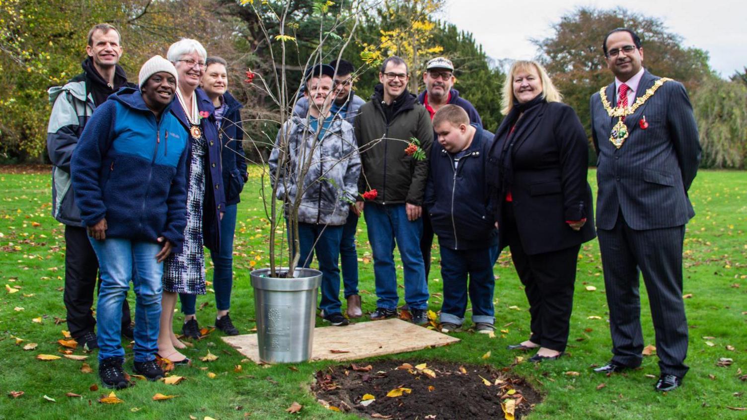 Dame Julie stood next to a sapling, alongside members of ArtWorks, a creative arts charity that works with adults who have learning disabilities.