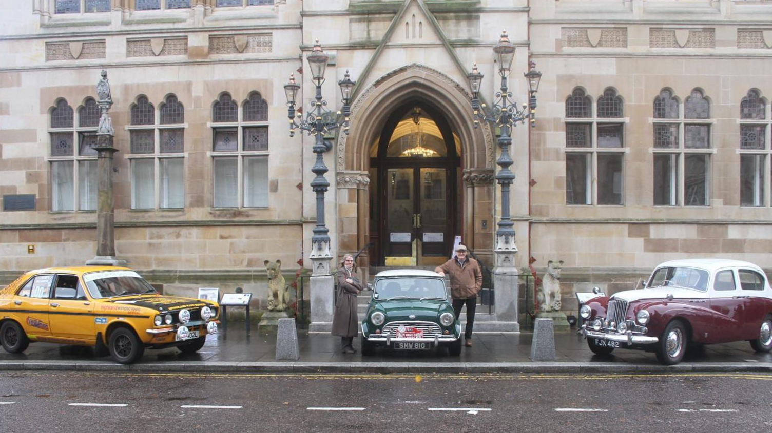 A yellow 1970s Hillman Avenger, green and white 1960s Mini Cooper and burgundy and white 1950 Sunbeam Talbot parked outside Inverness Town Hall on a wet day.