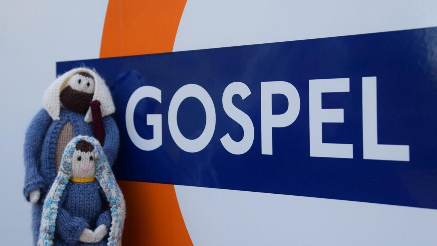 Miniature knitted figurine of Mary and Joseph next to a Gospel Oak station sign.