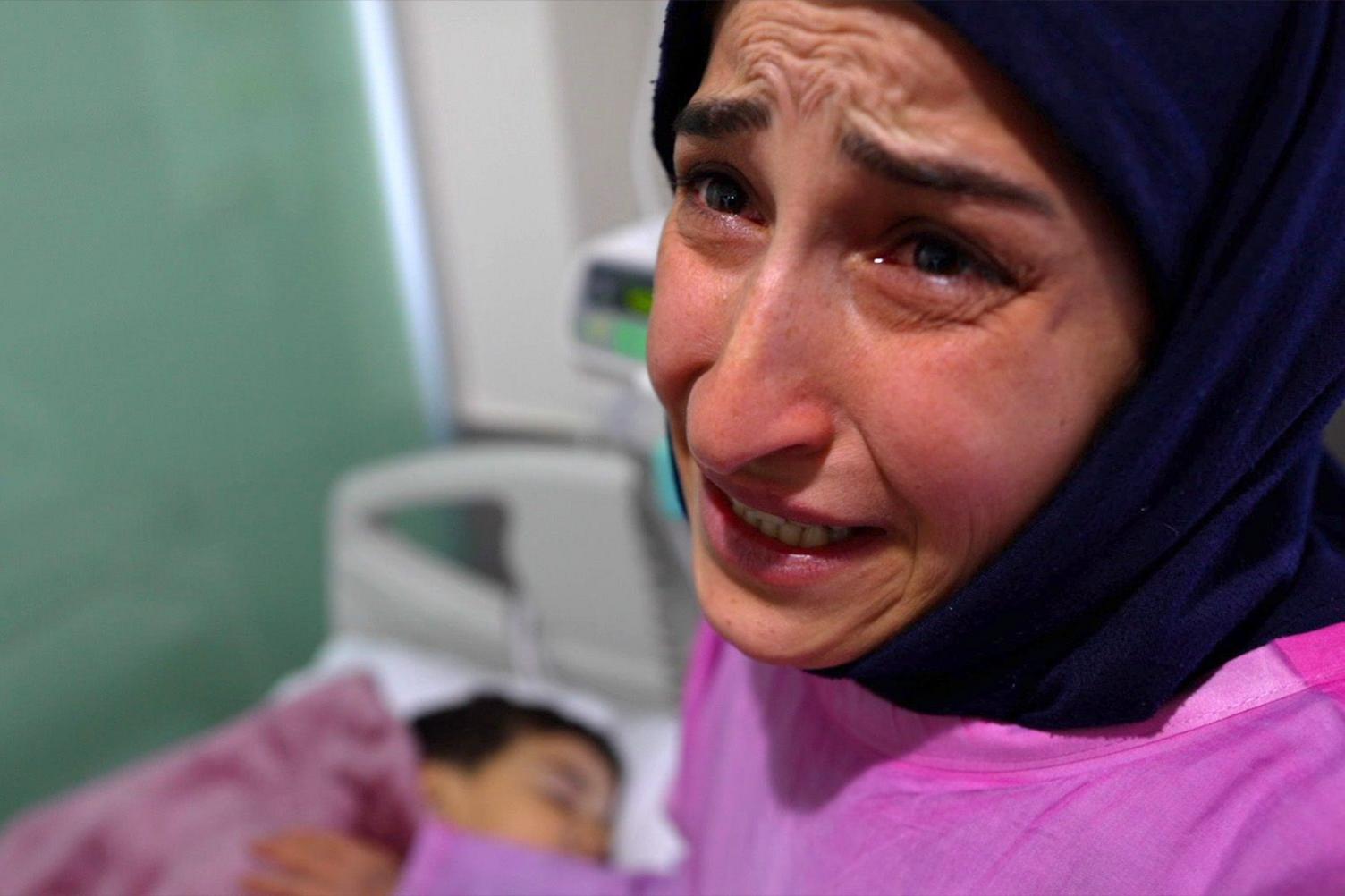 Najat is crying at the side of her son's hospital bed.