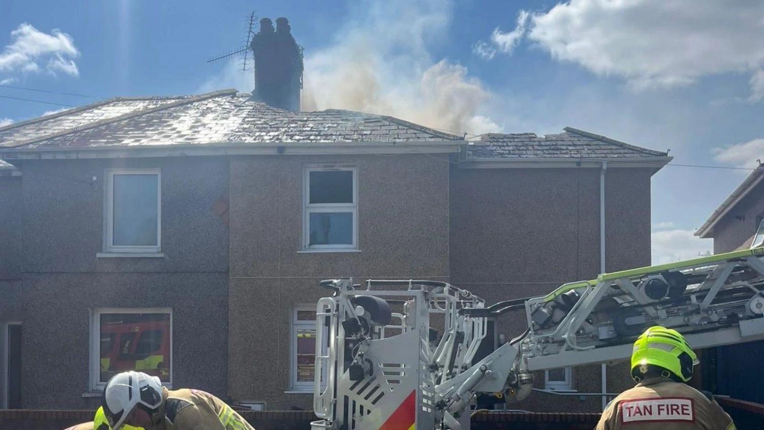 Firefighers and equipement outside a house fire at Brohawddgar, Llanelli. There is smoke rising from the roof of one of the houses. 