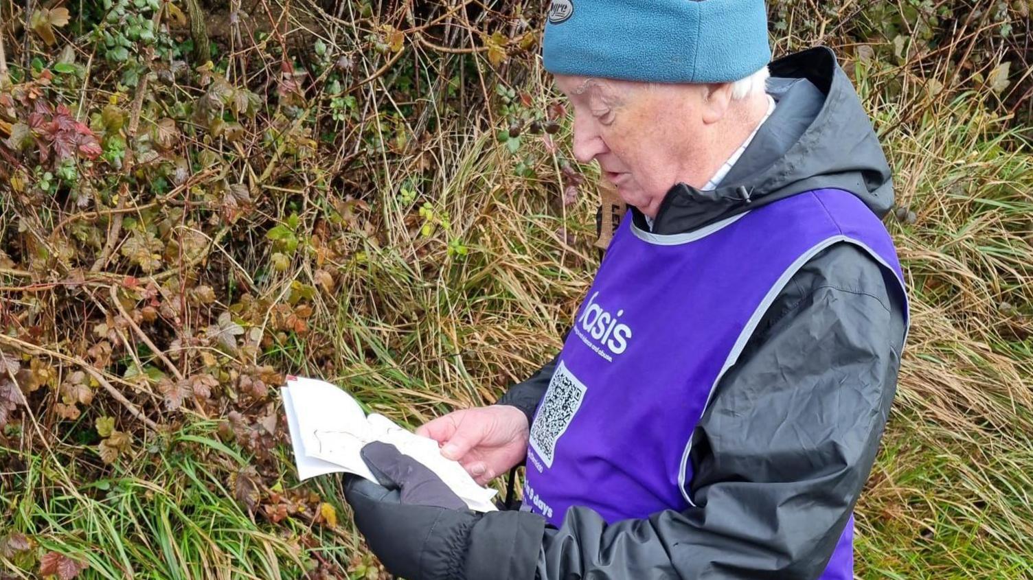 Close up shot of Derrick Downs wearing woolly hat and mauve bib reading a map