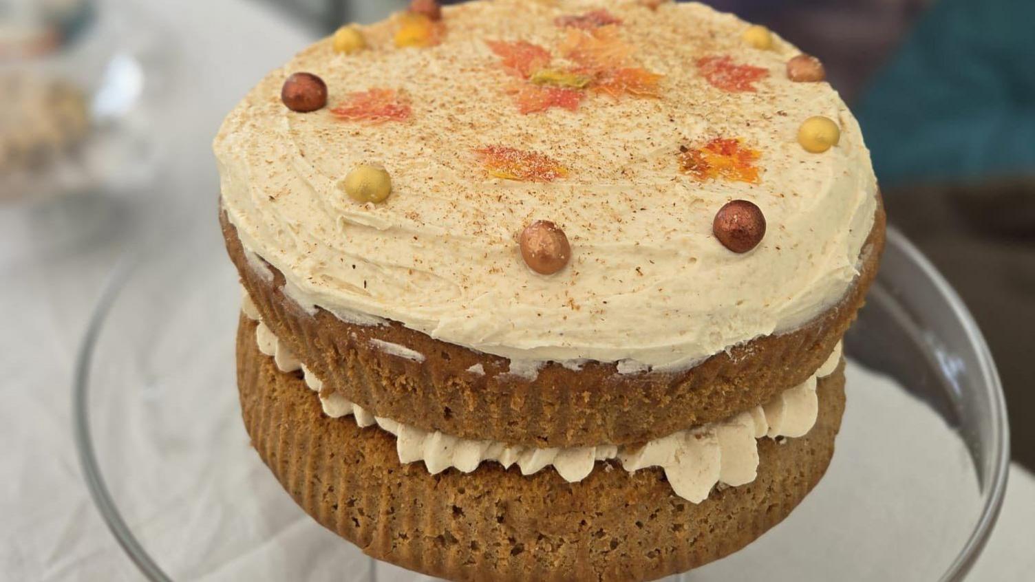 A cake with two tiers, each covered with a creamy rum butter spread. The top is decorated with cinemon and autumn leaves.