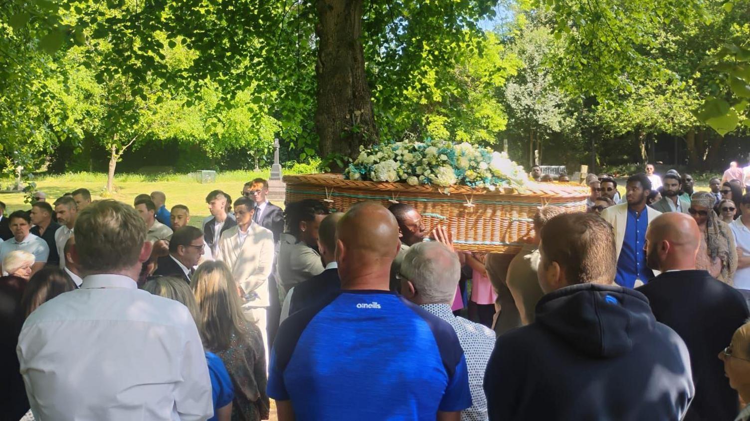 Pallbearers carry Joe Thompson's coffin as crowds of people look on.