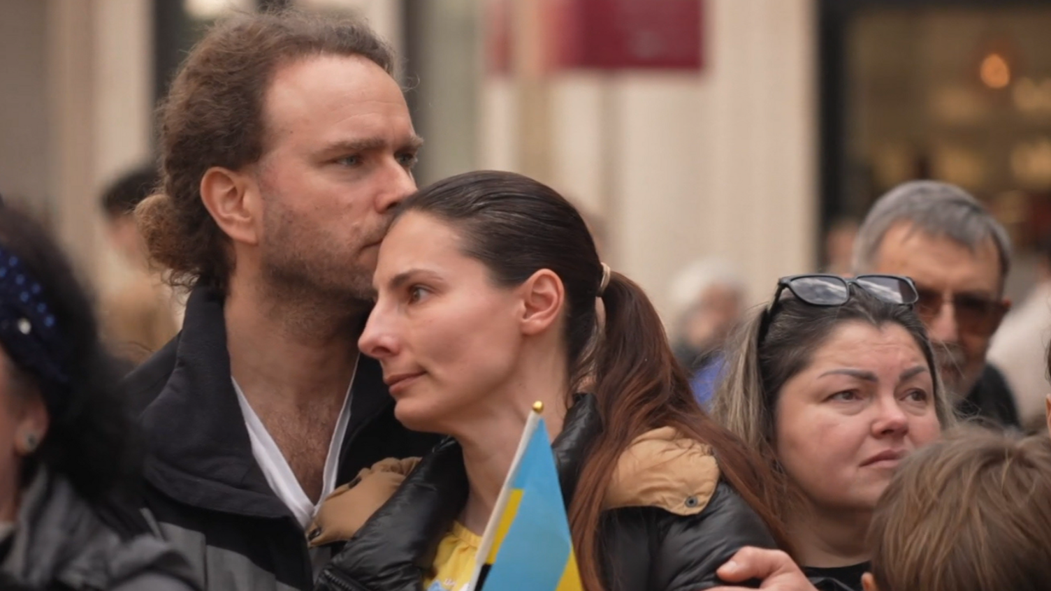 A man and a woman embrace at the Vigil. The woman is holding a small Ukrainian flag. 