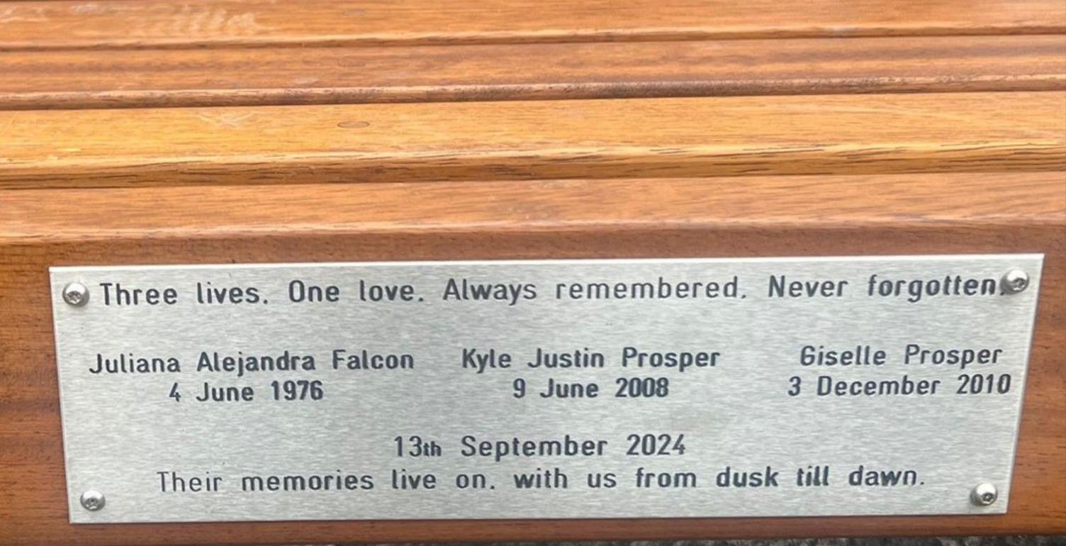 Silver plaque screwed on to a wooden slat with the words "Three lives, One love. Always remembered. Never forgotten" engraved in black above the names and dates of the three victims and the date of their deaths - 13th September 2024.