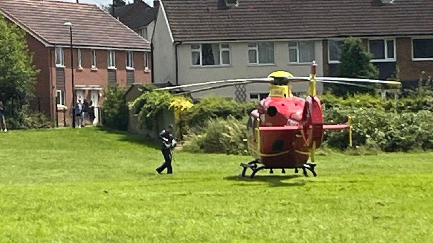 A red helicopter in a field with houses in the background