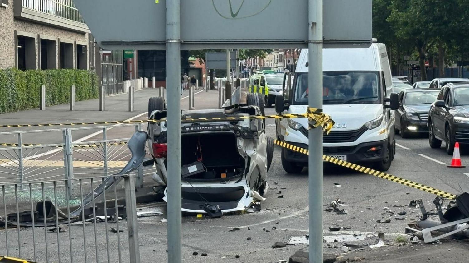 An overturned car at a city road junction, with cars and debris nearby