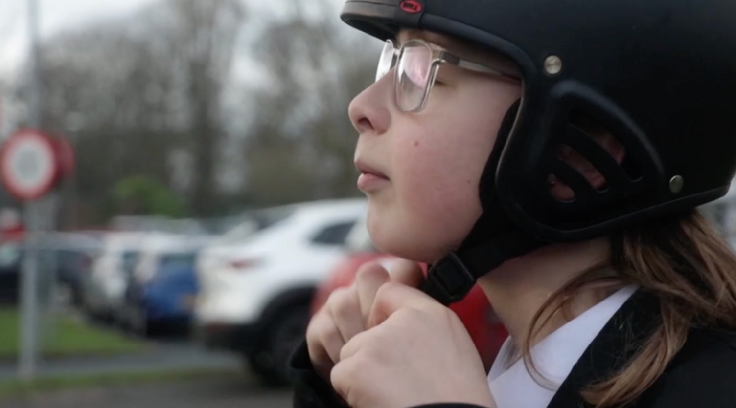 A boy with glasses fastens his safety helmet under his chin. 