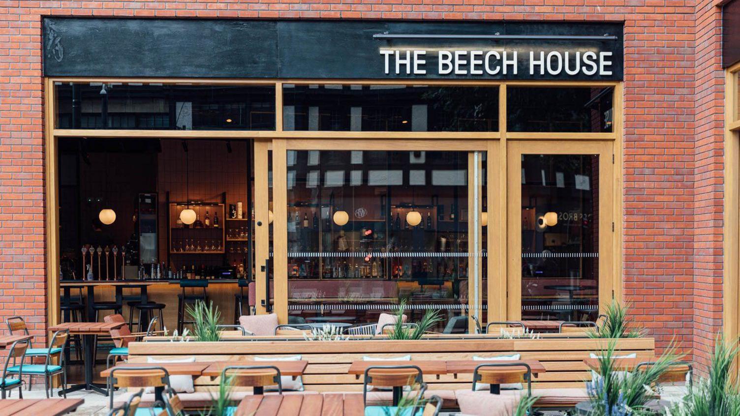 The outside of The Beech House, Watford, showing a business, with a bar in it, and tables and chairs outside. The building is red brick.