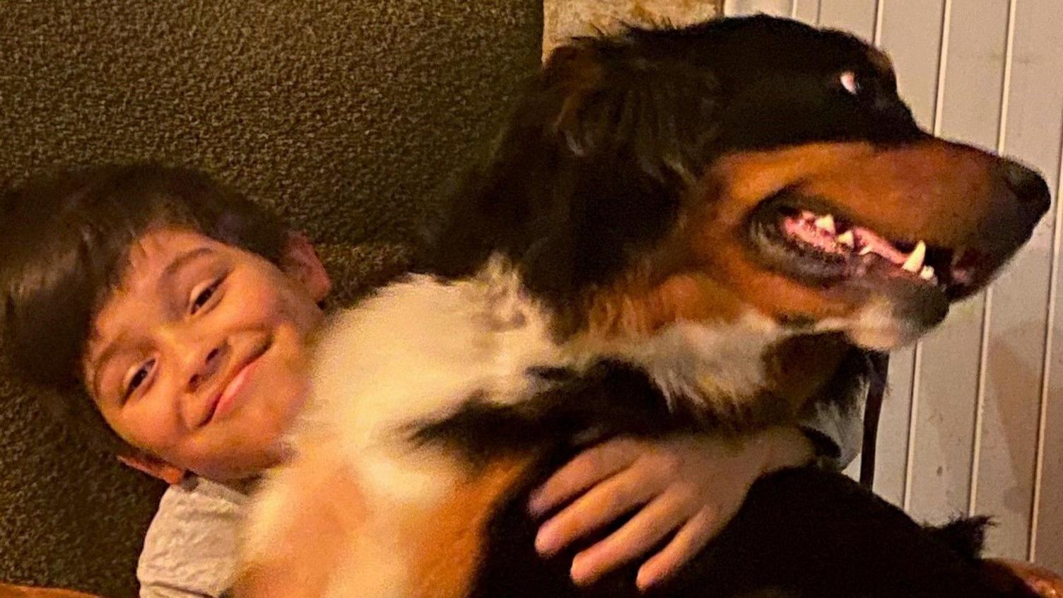 Young boy smiling at the camera with his arm around Mali the dog