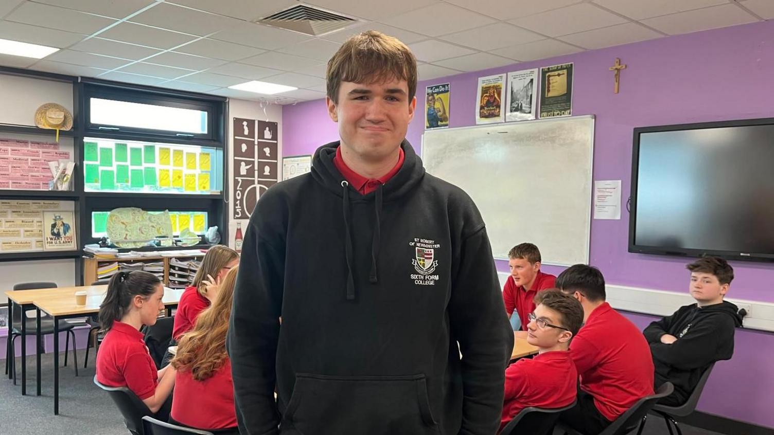 Angus wears a black school hoodie and his classmates are behind him in red tops