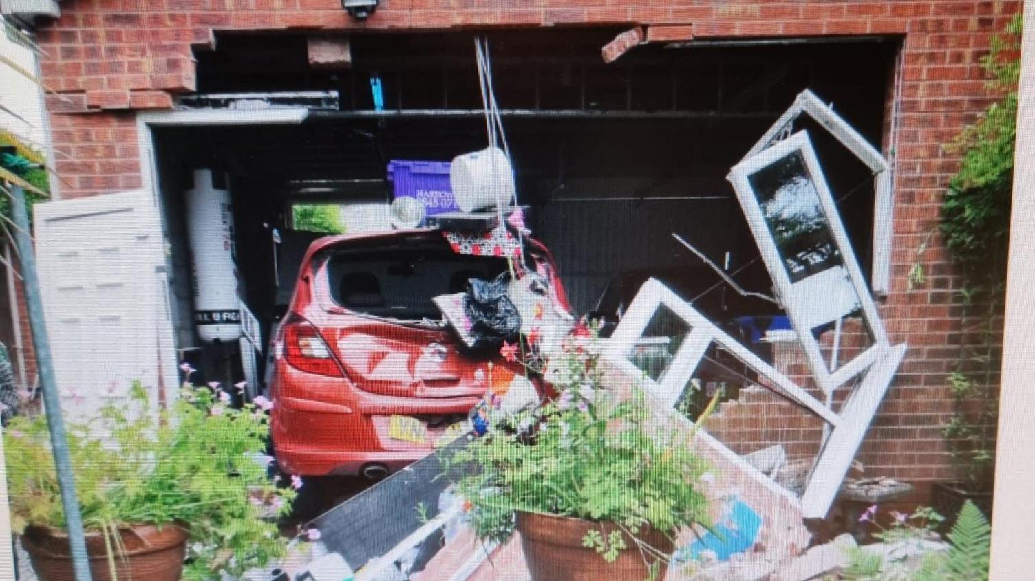 An image of a car bursting through a garage wall and into a garden