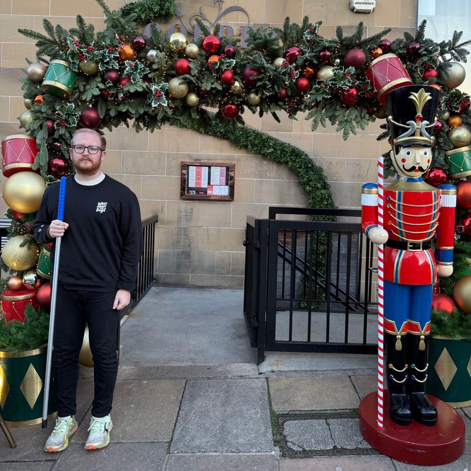 Mr Paxton is dressed in black and has ginger short hair and a beard and glasses. He is standing on the other side of the bar entrance to show where the stolen statue had been.