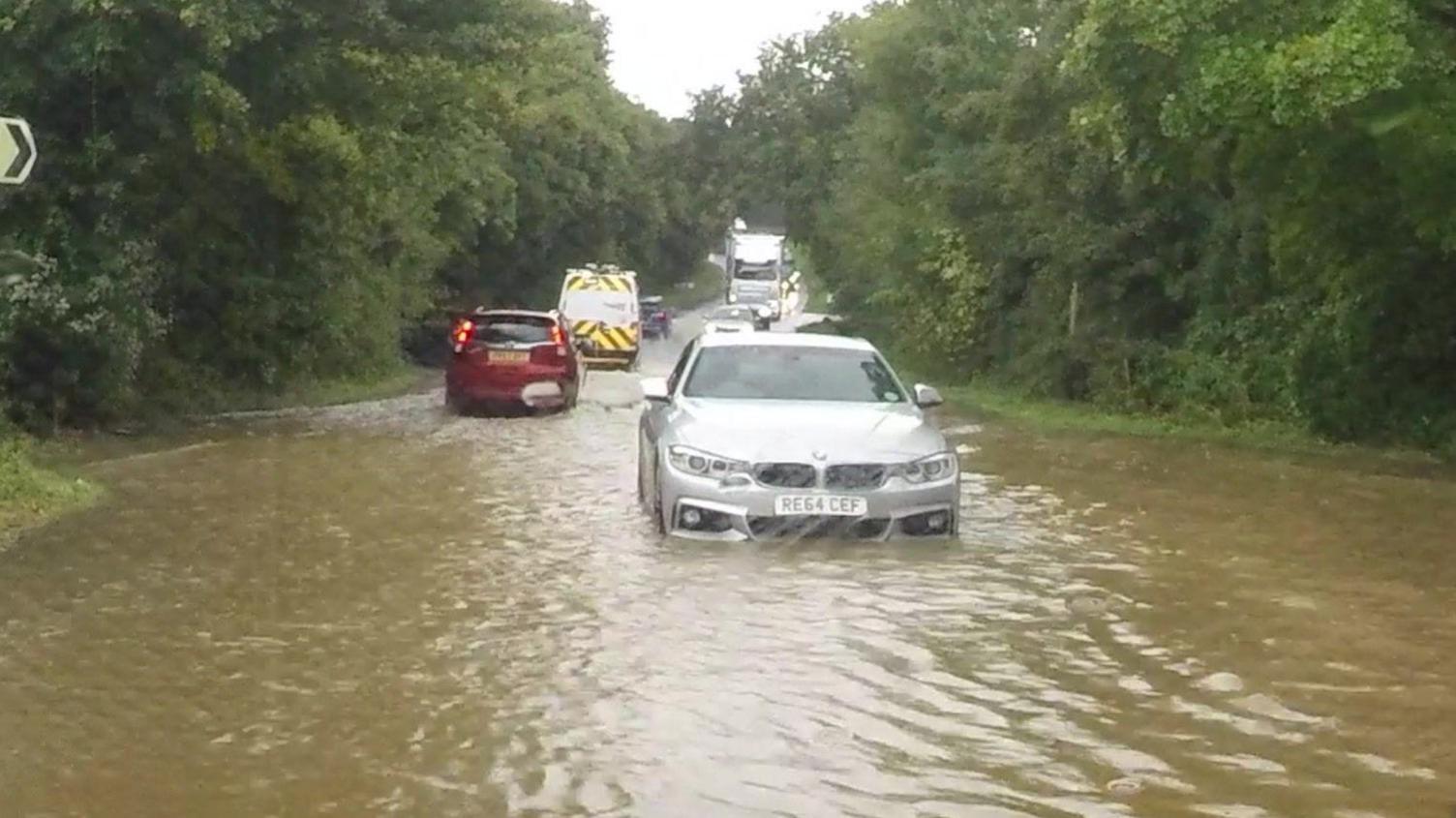 A car driving through deep muddy water, which is almost up to its number plate